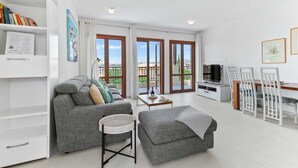 Una sala de estar moderna con un sofá gris, una mesita, un televisor y un comedor con sillas.