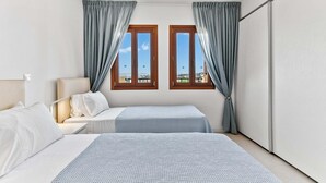 Habitación de hotel con dos camas, una mesita de noche, una lámpara y vistas a la ciudad a través de dos ventanas.