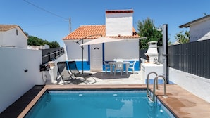 A swimming pool with a tiled deck, a covered seating area with a table and chairs, and a white building with a red-tiled roof. - Alentejo Poolside By Gt House (São Domingos de Ana Loura)