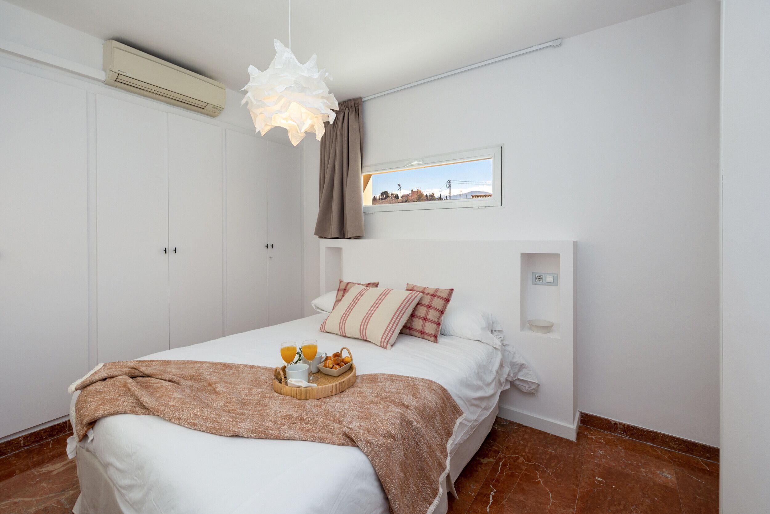 Un dormitorio con cama, mesita de noche, ventana y aire acondicionado instalado en la pared.