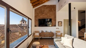 A living room with a large window, a brick wall, a TV, a sofa, and a wooden coffee table. - ChezmoiHomes Santiago Duplex Penthouse (Granada)