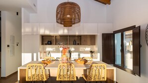 A modern kitchen with a central island, wicker chairs, and a hanging light fixture. - ChezmoiHomes Santiago Duplex Penthouse (Granada)