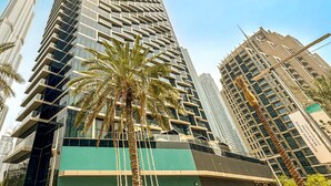 A tall, modern skyscraper with a unique facade, surrounded by palm trees and other high-rise buildings. - HiGuests - Address Opera Residences (Dubai)
