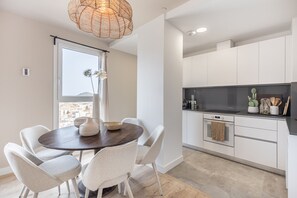 A modern kitchen with white cabinets, a dark countertop, and a hanging light fixture.