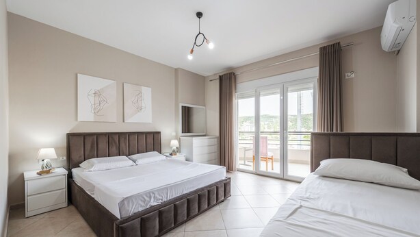 A modern hotel room with a large bed, a TV, a balcony with curtains, and artwork on the wall. - Kondo Stays - City Center Apartments (Vlorë)