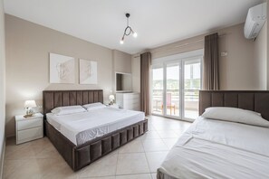 A modern hotel room with a large bed, a TV, a balcony with curtains, and artwork on the wall. - Kondo Stays - City Center Apartments (Vlorë)