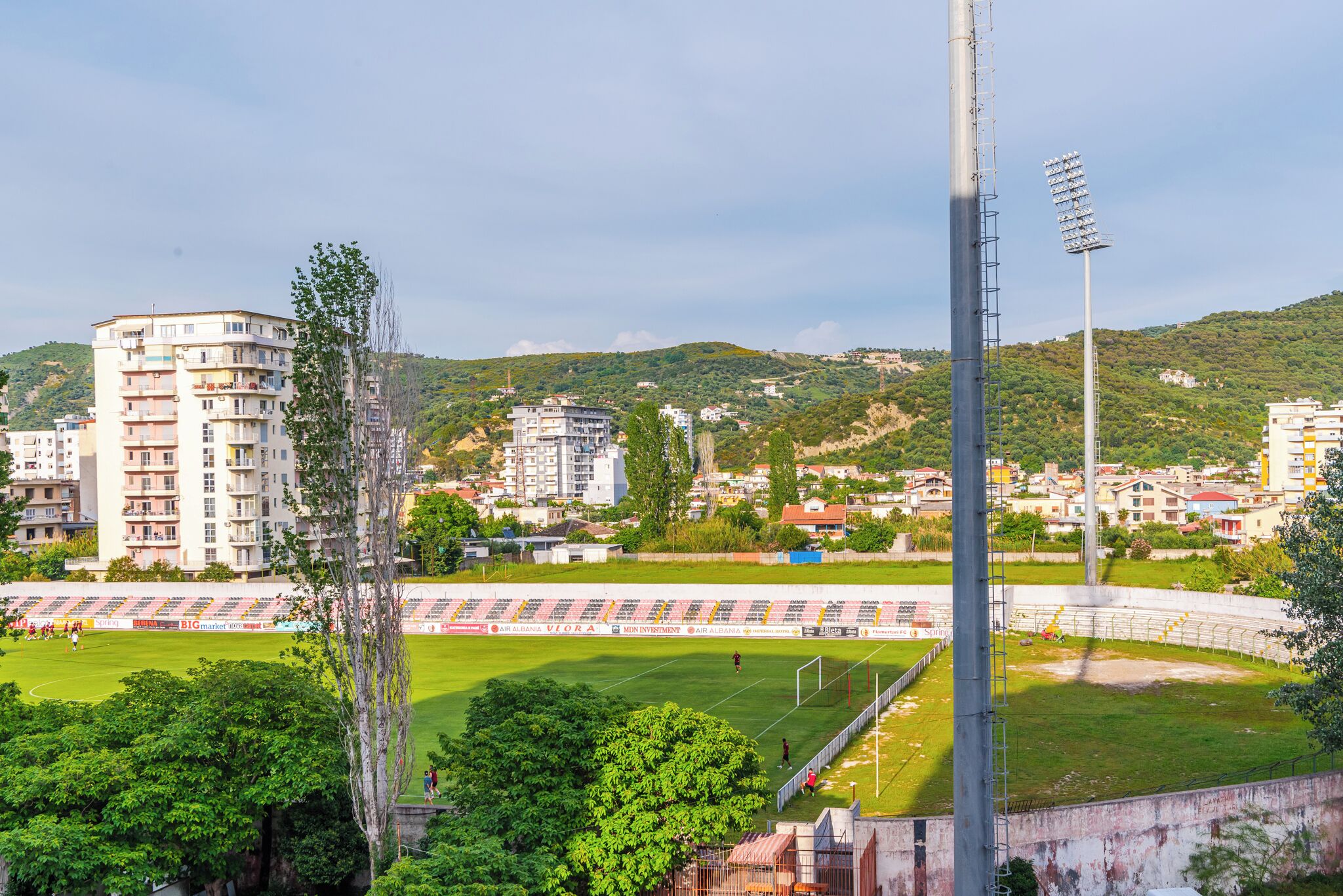 Een stadion met een groen veld, toeschouwersplaatsen en omliggende gebouwen.
