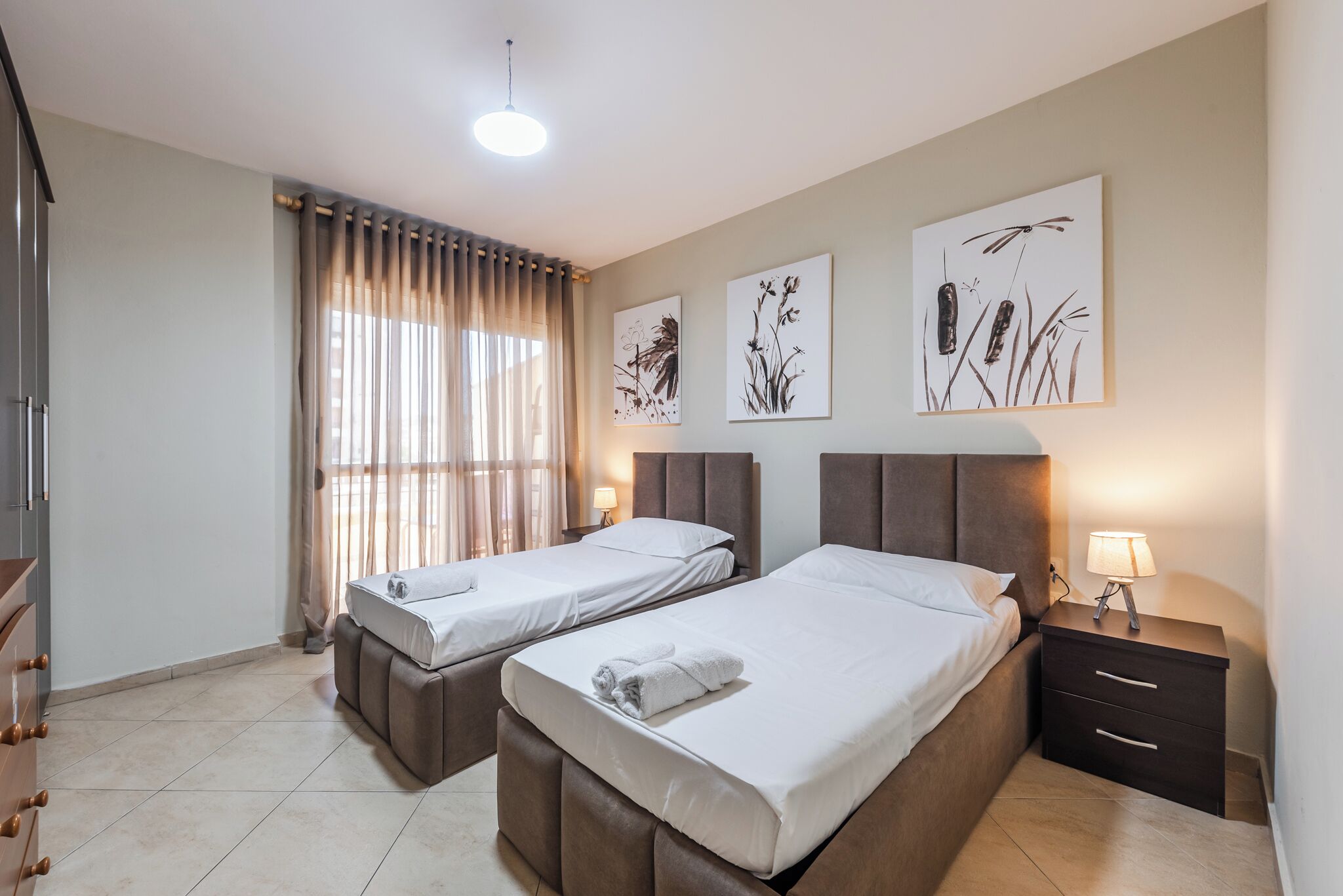 A hotel room with two beds, a nightstand, a dresser, and artwork on the walls.