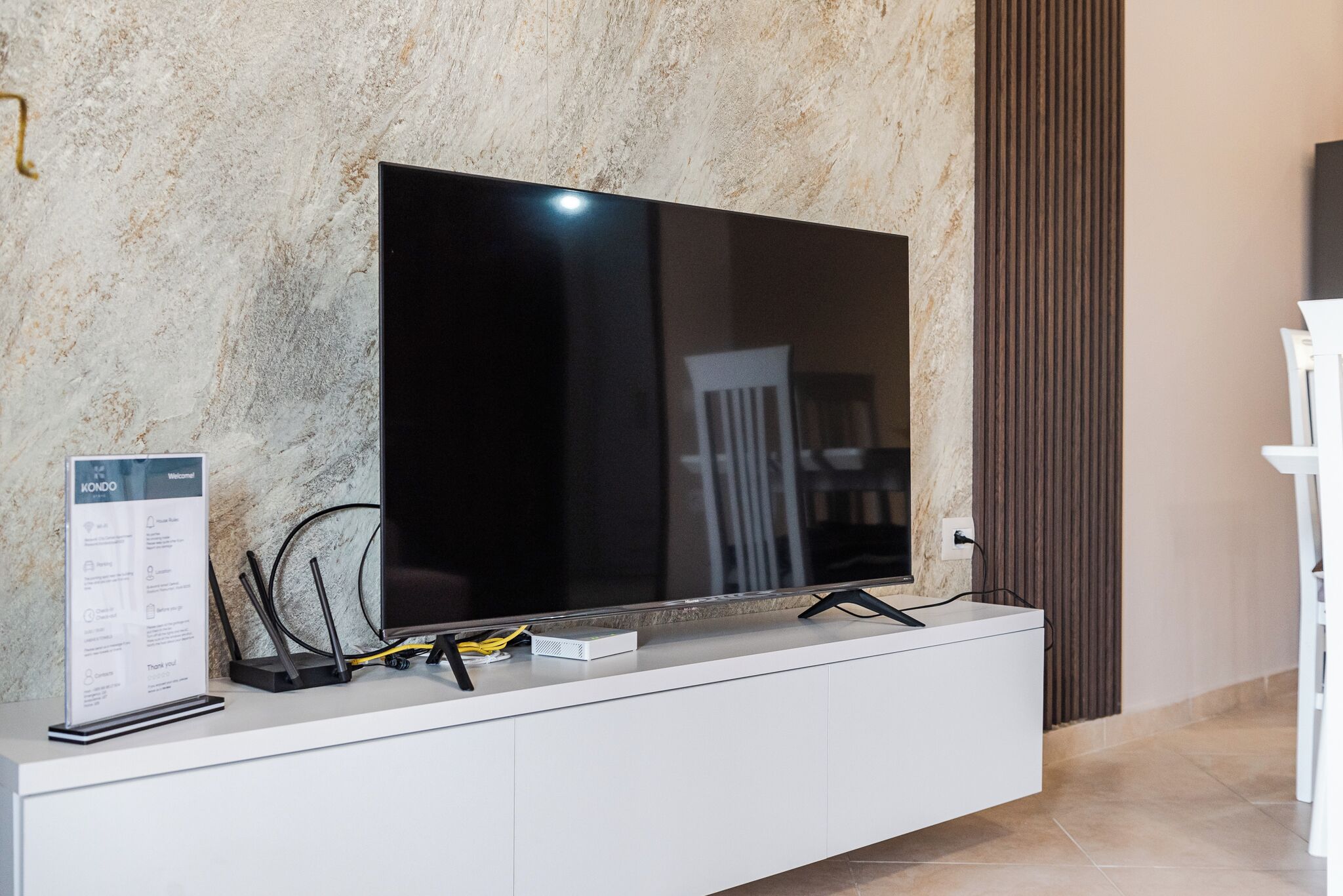 Een flatscreen-televisie bevestigd aan een wit kastje, met een marmeren wand erachter.