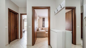A hallway with wooden doors, a white radiator, and a beige sofa in the background. - Kondo Stays - City Center Apartments (Vlorë)