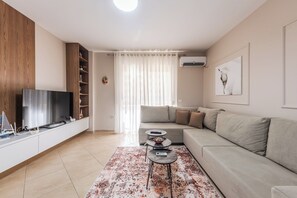 A modern living room with a flat-screen TV, a sofa, a coffee table, and a decorative rug. - Kondo Stays - City Center Apartments (Vlorë)