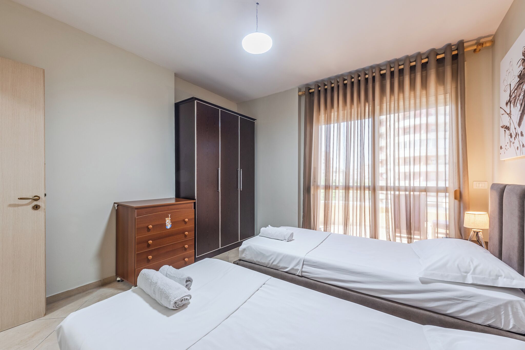 Una habitación de hotel con dos camas, un armario y un gran ventanal con cortinas.
