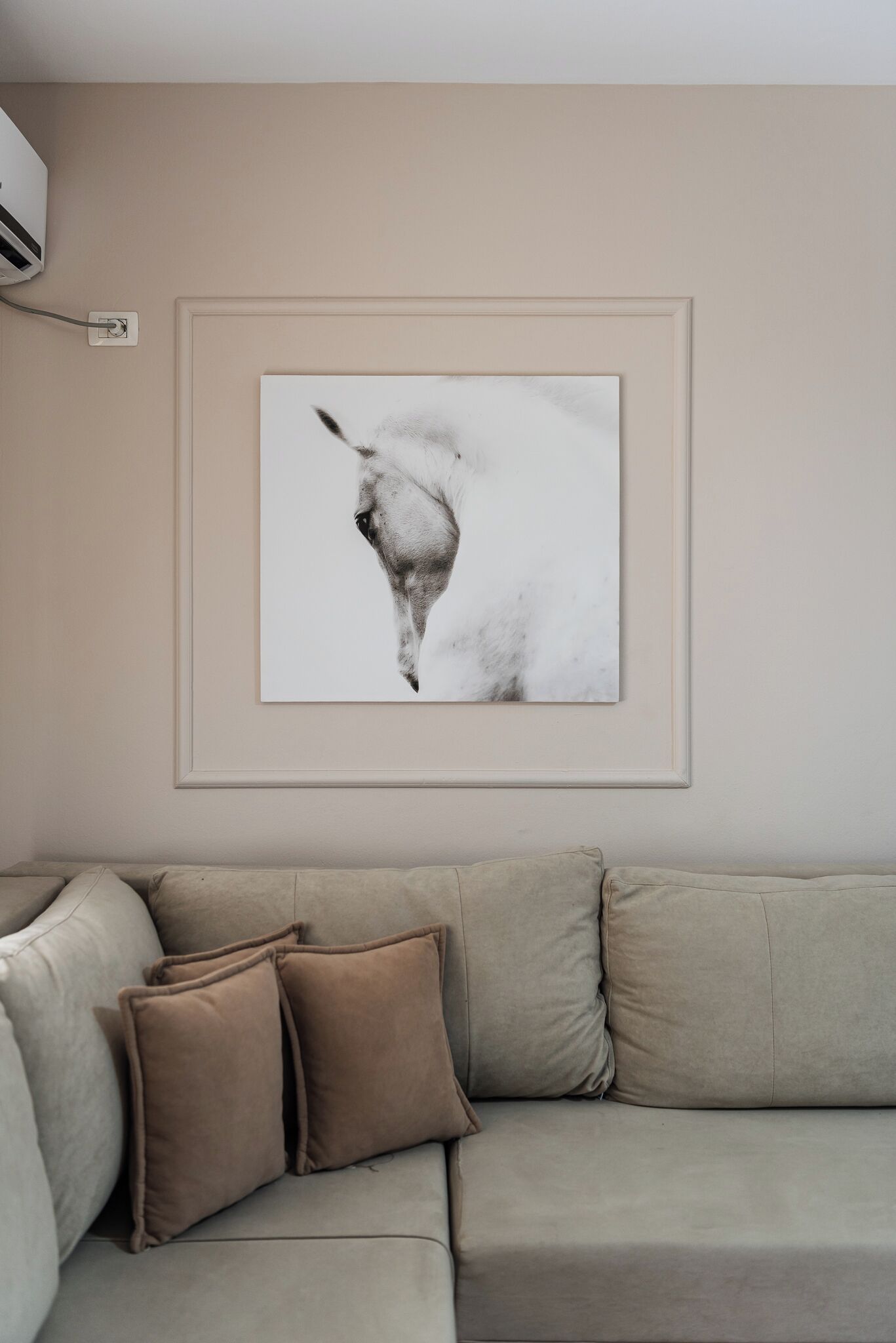 A beige sofa with three cushions and a framed abstract artwork on the wall.