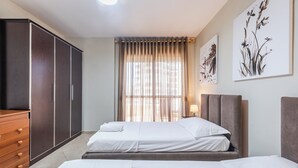 A hotel room with two beds, a wardrobe, a window with curtains, and wall art. - Kondo Stays - City Center Apartments (Vlorë)