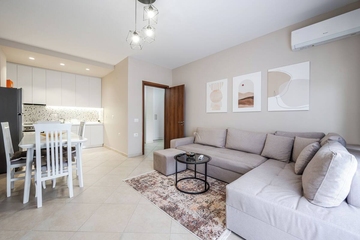 A modern living room with a sofa, a dining table with chairs, and a kitchen in the background.