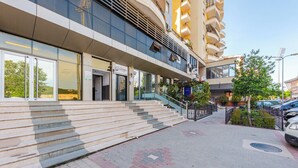 A modern building with a glass facade, a set of outdoor stairs leading to the entrance, and a parking area with cars. - Kondo Stays - City Center Apartments (Vlorë)