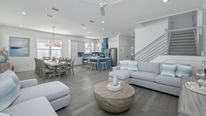A spacious living area with a dining set, a sofa, and a round coffee table. - Seaspray: Pool! Sleeps 26! Beach access! (Destin)