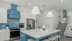 A modern kitchen with white cabinets, a blue island, stainless steel appliances, and pendant lighting. - Seaspray: Pool! Sleeps 26! Beach access! (Destin)