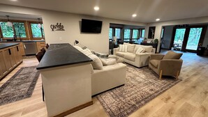 A modern kitchen with a large island, a dining area with a sofa and chairs, and a living room with a large couch and a TV.