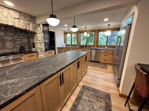 A modern kitchen with a granite countertop, wooden cabinets, a stone accent wall, and large windows.