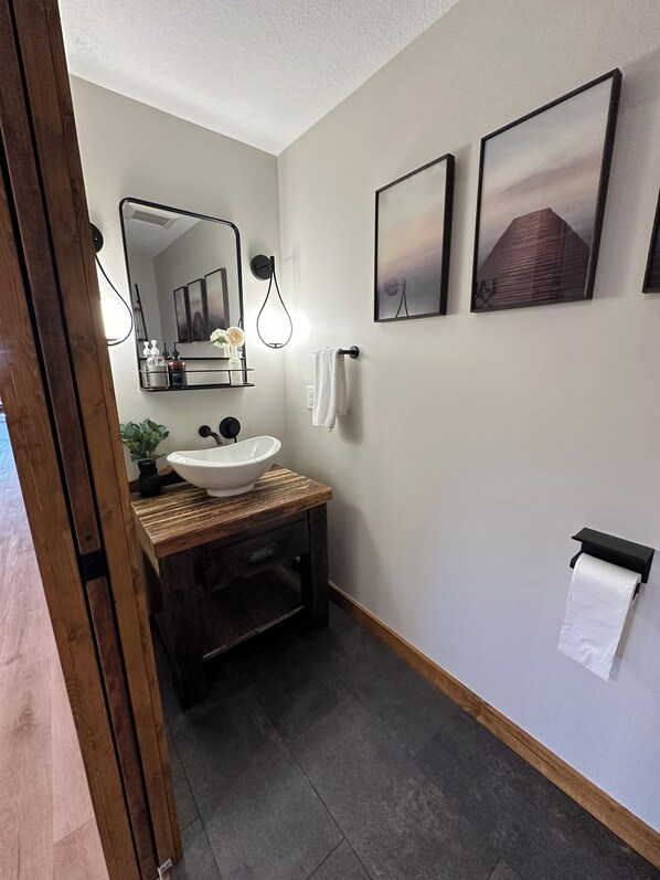 A bathroom with a wooden vanity, a white sink, a mirror, and two framed pictures on the wall.
