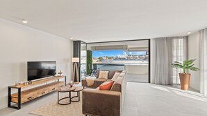 Ein modernes Wohnzimmer mit einem großen Flachbildfernseher, einer Holz-Unterhaltungseinheit, einem braunen Sofa und Blick auf eine Stadtlandschaft durch große Fenster.