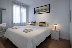 A hotel room with a large bed, two bedside tables, a nightstand, a lamp, a painting, and a window with sheer curtains. - Habitat Apartments Teatre 12 (Barcelona)