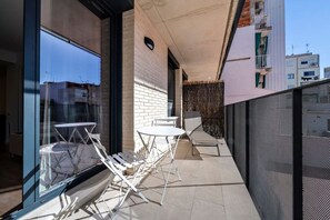 An outdoor balcony with a table and chairs, a glass door, and a view of the city.