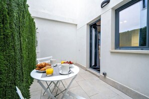 A small outdoor dining area with a table, chairs, and breakfast items including croissants and orange juice.