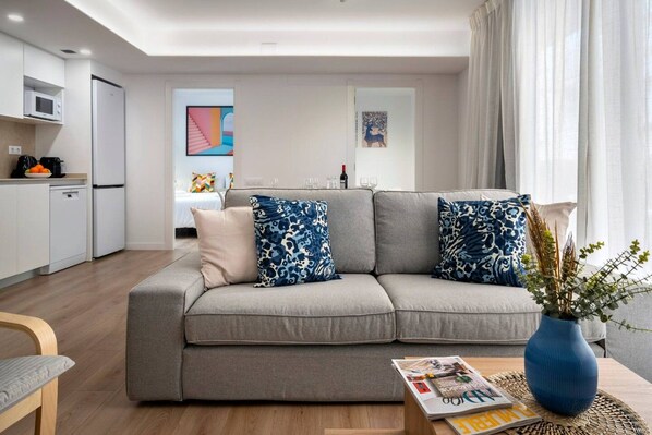 A modern living room with a grey sofa, two patterned cushions, a magazine on a side table, and a vase with plants.