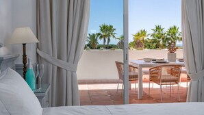 A hotel room with a bed, a nightstand, a lamp, and a view of an outdoor balcony with a table and chairs.