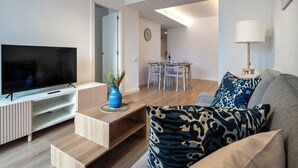 A modern living room with a flat-screen TV, wooden entertainment unit, and a sofa with patterned cushions. - Habitat Apartments Teatre 22 (Barcelona)
