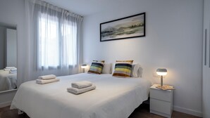 A neatly made bed with white linens and two pillows, a bedside table with a lamp, and a framed landscape painting on the wall. - Habitat Apartments Teatre 22 (Barcelona)