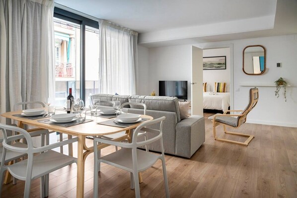 A modern living room with a dining area, a grey sofa, a TV, and a wooden floor.
