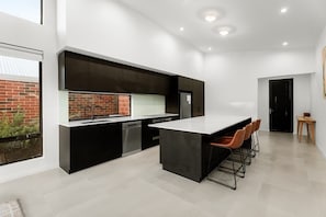 Une cuisine moderne dotée d’un grand îlot central, de meubles de couleur noire et offrant une vue sur un mur en briques.