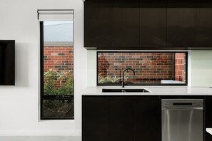 Une cuisine moderne dotée d’un lave-vaisselle encastré, d’une fenêtre donnant sur un mur de briques et sur de la verdure, et d’un meuble noir.