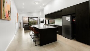 Une cuisine moderne dotée d’un îlot central, de meubles de rangement noirs et d’un grand réfrigérateur.