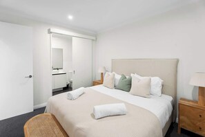 Ein Hotelzimmer mit Bett, Nachttisch aus Holz, Stuhl, Badezimmer mit Spiegel und Tür.