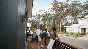 Une terrasse en bois avec des personnes, un bâtiment moderne et des arbres en arrière-plan.