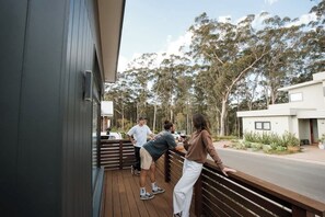 Eine Holzterrasse mit Personen, ein modernes Gebäude und Bäume im Hintergrund.