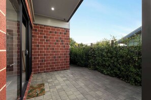 A patio area with a brick wall, a glass door, and a hedge.