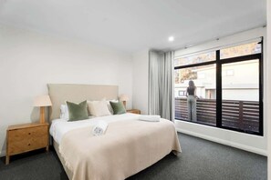 Ein Hotelzimmer mit Bett, Nachttisch, einem Fenster mit Vorhängen und Blick nach draußen.