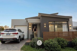 Un bâtiment moderne avec une voiture garée devant, une personne qui entre et un banc au premier plan.