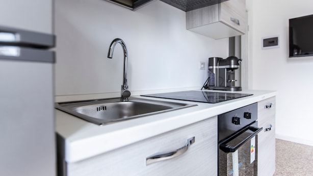 Una cocina moderna con un lavamanos de acero inoxidable, un horno empotrado y una cafetera.