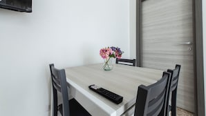 Una mesa de comedor con un jarrón de flores, un control remoto y cuatro sillas.