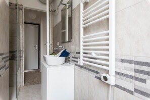 Un baño con lavamanos blanco, cabina de ducha de vidrio y un perchero para toallas.