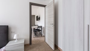 Habitación de hotel con cama, mesita de noche con lámpara, puerta que da a un comedor y un equipo de aire acondicionado en la pared.