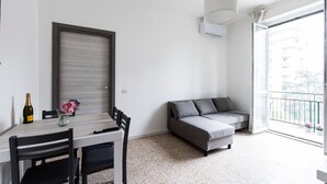 Una sala de estar moderna con una mesa de comedor, sillas, un sofá y un amplio ventanal con balcón.