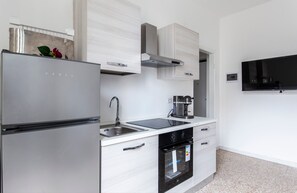 A modern kitchen with a built-in refrigerator, stainless steel sink, and a flat-screen TV mounted on the wall. - Bilocale Noverasco IEO 3 (Opera)