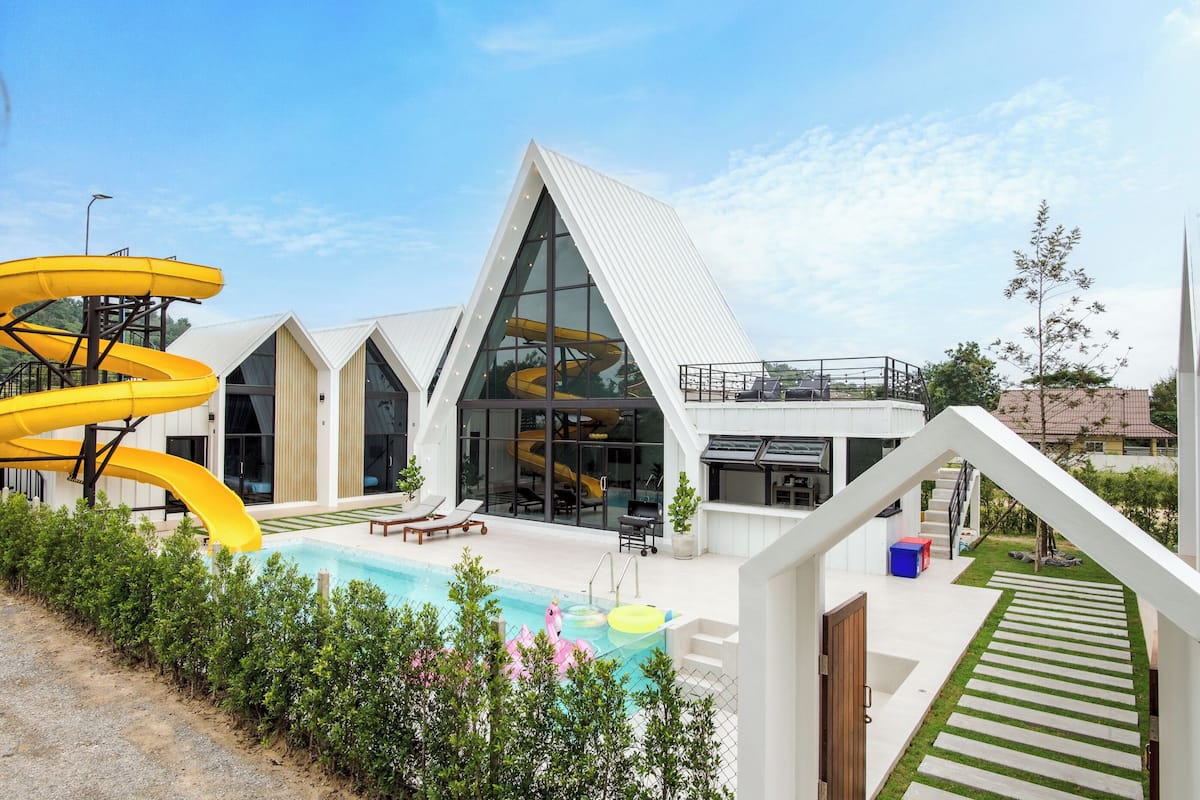 A modern building with a pool, yellow slides, and a clear sky.